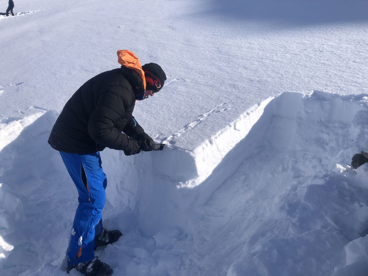A man stands next to a snowpack, checking the stability of the snow layers.