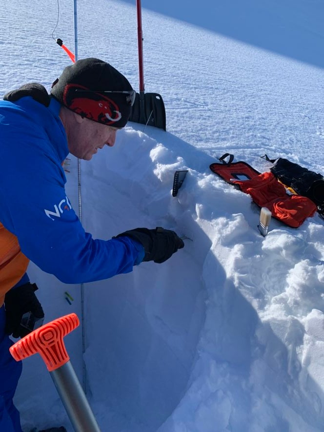 Mann står i et vinterlandskap og ved en snøskavl. Han måler stabiliteten i snølagene.