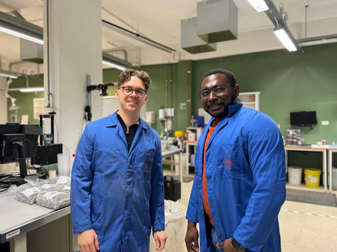 Fredrik og Jacob iført blå labfrakker. I bakgrunnen ser man typiske laboratorieteknisk utstyr.
